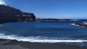 A coastal scene with a rocky cliff and a beach. - Near the Drago in Icod (Icod de los Vinos)