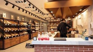 A bakery with shelves of baked goods, a brick counter, and a person preparing food. - Near the Drago in Icod (Icod de los Vinos)