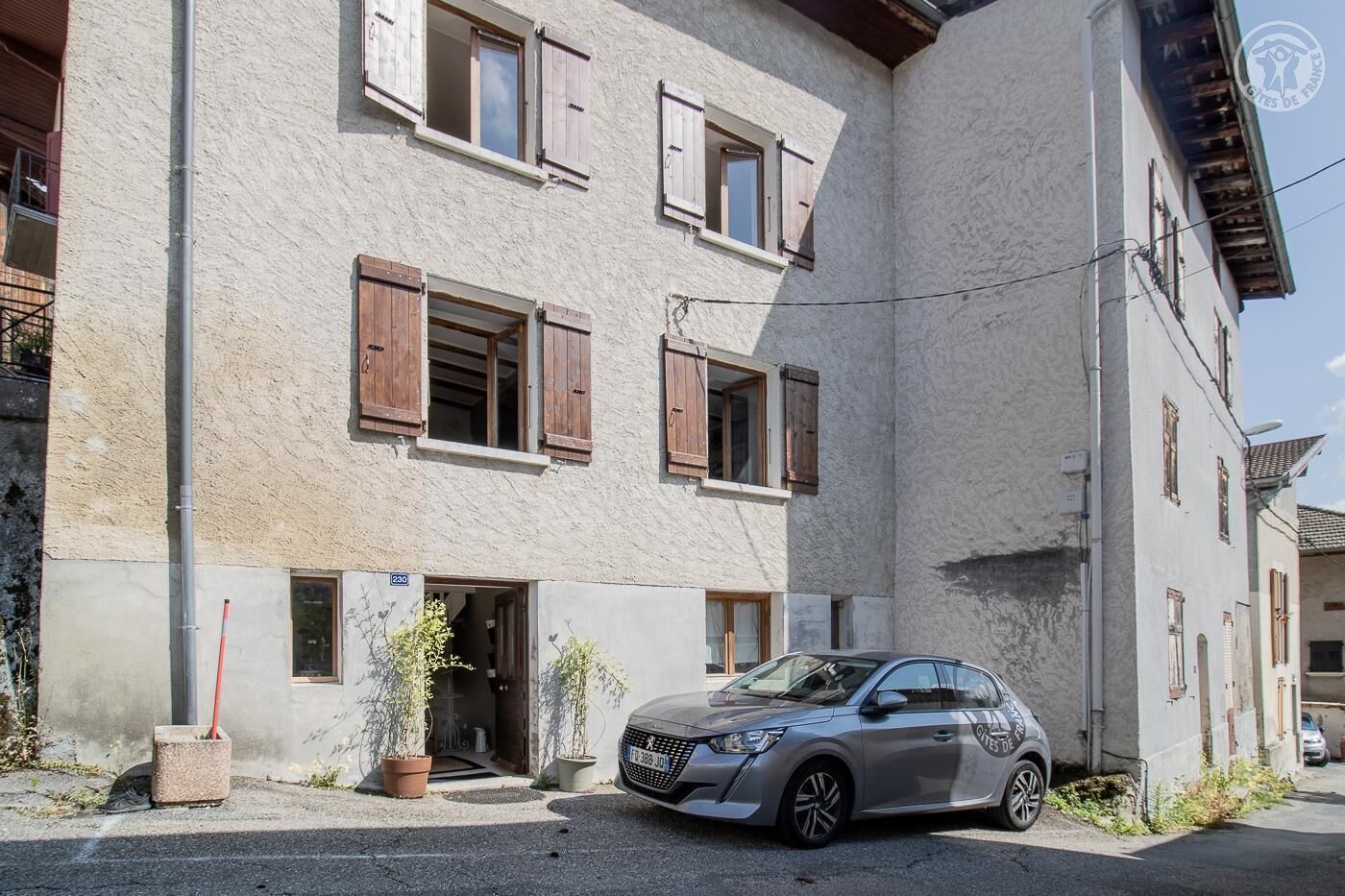 Un bâtiment à deux étages avec des volets en bois, une voiture garée et des plantes en pot.