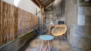 A cozy outdoor seating area with a table and two chairs, a bamboo fence, and a stone wall. - LA P'tite Pierrue - Arvillard (ARVILLARD)