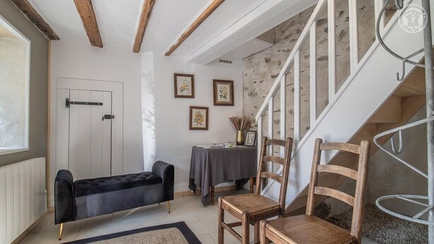 A cozy room with a black sofa, wooden chairs, a small table with a vase, and a staircase. - LA P'tite Pierrue - Arvillard (ARVILLARD)