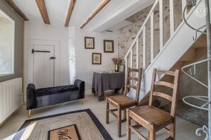 Una habitación acogedora con un sofá negro, sillas de madera, una mesita con un jarrón y una escalera.