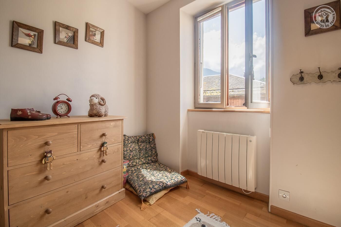 Una habitación con un aparador de madera, una silla estampada, un radiador y una ventana con vistas a montañas.