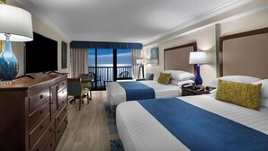 Habitación de hotel con dos camas, un escritorio, un televisor y un balcón con vista al mar.