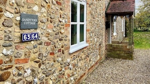 Una cabaña de piedra con un letrero que dice 'Sandytoes Cottage' y el número de casa '6364'.