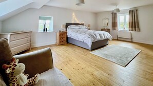 Un dormitorio con techo inclinado, cama con cabecera, cómoda, mesita de noche, ventana con cortinas y un peluche.