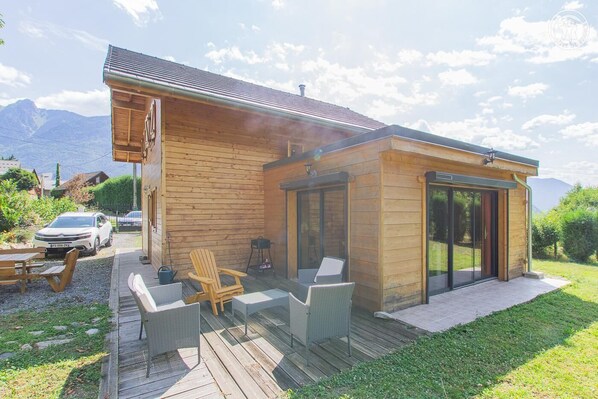 A wooden cabin with a deck, outdoor seating, and a car parked nearby. - Chez Cathy - Saint Remy DE Maurienne (SAINT REMY DE MAURIENNE)