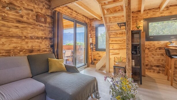 L’intérieur d’un chalet en bois chaleureux et accueillant, avec un canapé, une table à manger et un escalier menant à un espace extérieur.