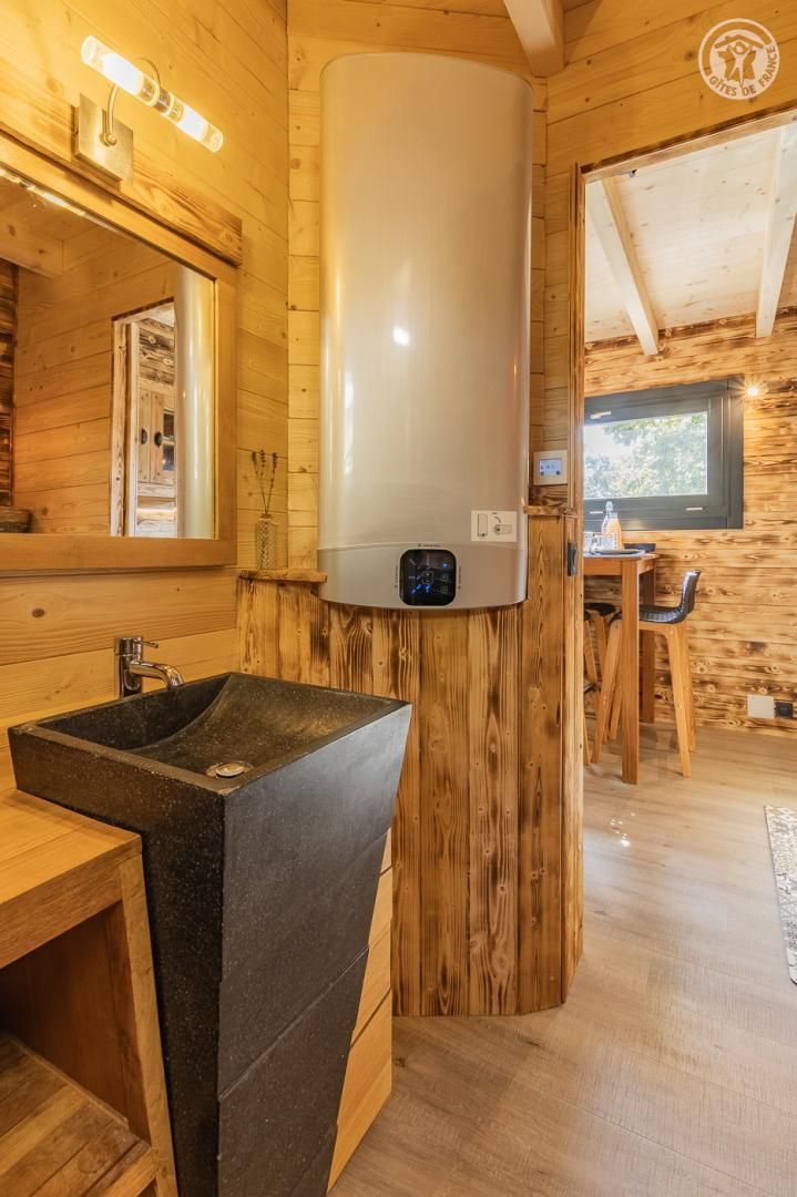 A wooden interior with a large white water heater, a black sink, and a wooden dining table.