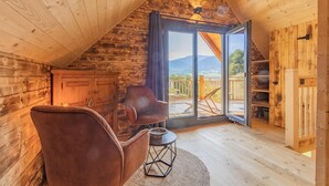 Un chalet confortable avec un intérieur en bois et une grande porte-fenêtre coulissante donnant sur une terrasse avec vue sur les montagnes.