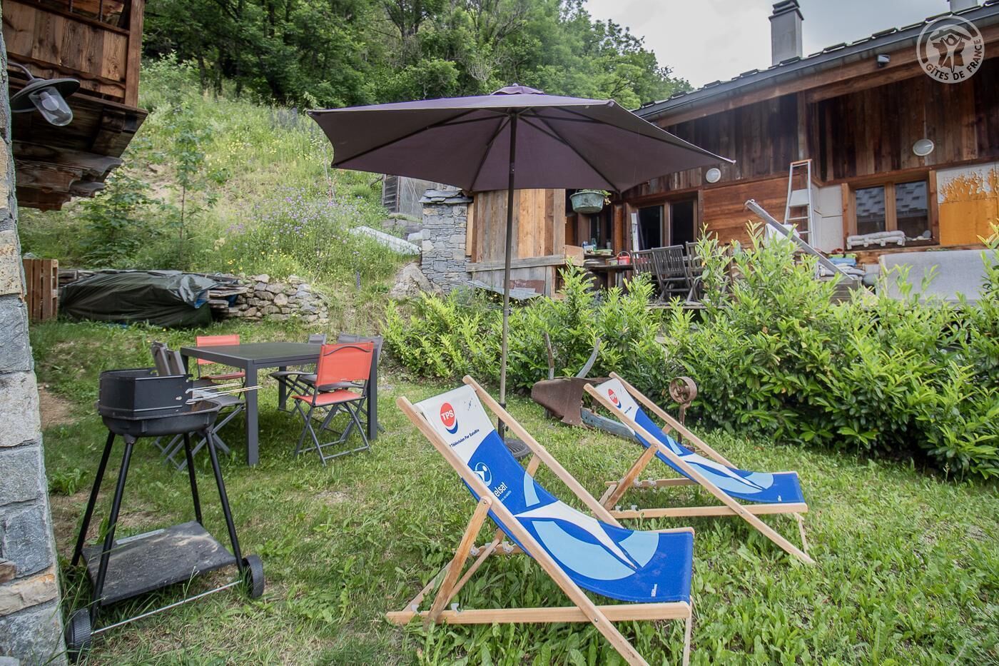 An outdoor seating area with a table and chairs, a barbecue grill, and a large umbrella.