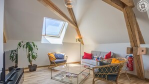 A cozy loft apartment with a sloped ceiling, a skylight, a glass coffee table, wicker furniture, and a fire extinguisher. - LA Cure Gourmande - LA Sure (SAINT CHRISTOPHE LA GROTTE)