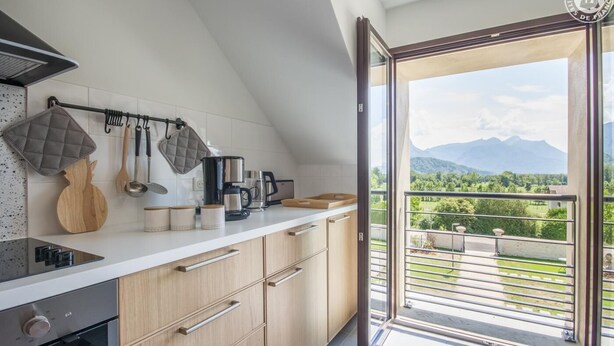 A modern kitchen with wooden cabinets, a built-in oven, and a coffee maker. A large window offers a view of a balcony with a mountain backdrop. - LA Cure Gourmande - LA Sure (SAINT CHRISTOPHE LA GROTTE)