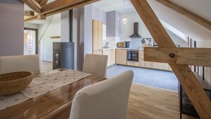 A modern loft apartment with exposed wooden beams, a dining area with a wooden table and chairs, a kitchen with a stove and cabinets, and a large window providing natural light. - LA Cure Gourmande - LA Sure (SAINT CHRISTOPHE LA GROTTE)
