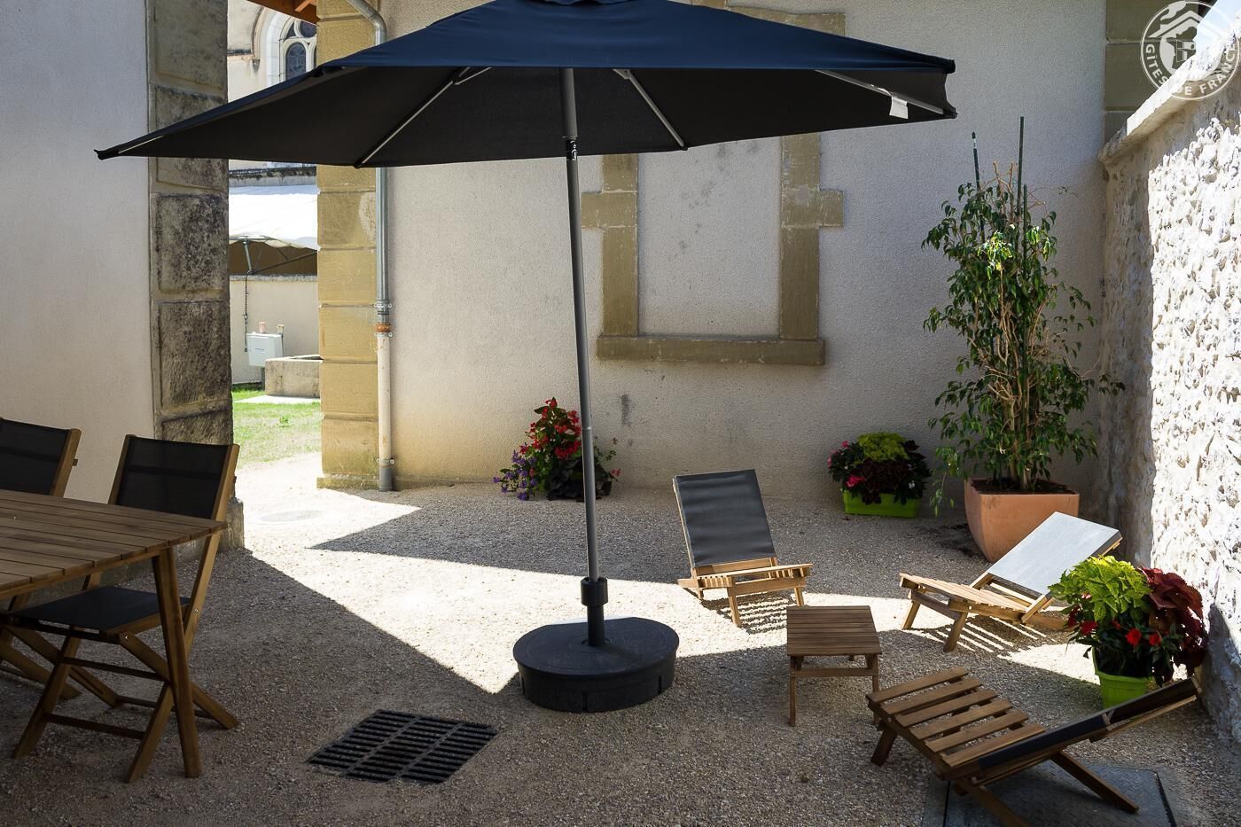 An outdoor patio with a table and chairs, a large umbrella, and potted plants.