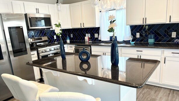 Una cucina moderna con mobili bianchi, un'isola centrale con posti a sedere, elettrodomestici in acciaio inossidabile e vasi decorativi.
