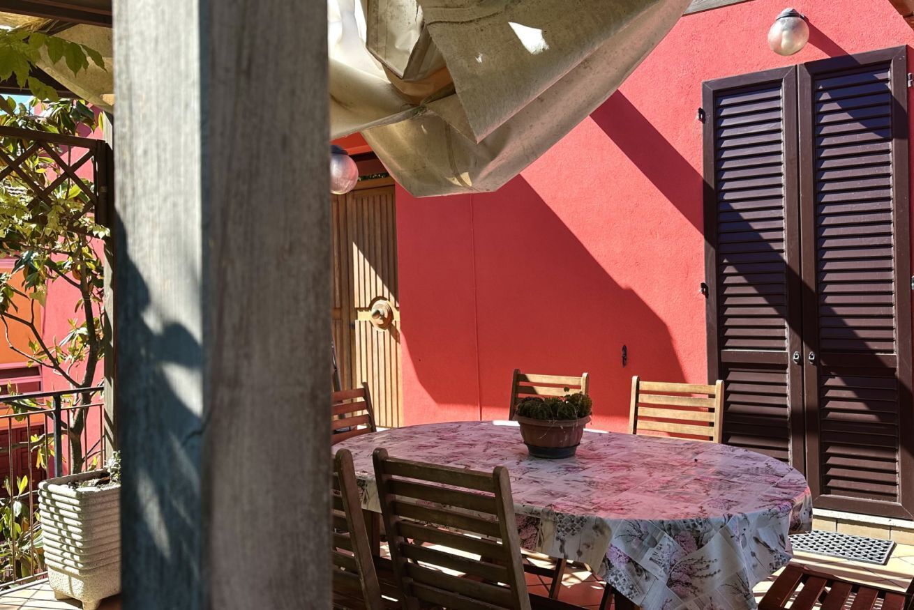 Une table ronde entourée de chaises, une plante en pot et un mur rouge avec des volets.