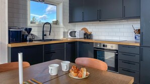 A modern kitchen with dark cabinets, a wooden countertop, a sink, a microwave, and an oven. There is a dining table with two white mugs and a plate of food. - 2 bedroom cozy home in årjäng (Årjäng)