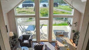 A spacious room with large windows, a wooden ceiling, and a view of a lake and buildings. - 2 bedroom cozy home in årjäng (Årjäng)