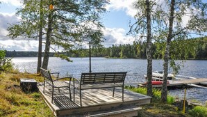 A wooden dock with benches overlooking a calm lake, surrounded by trees and a docked boat. - 2 bedroom cozy home in årjäng (Årjäng)