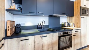 Une cuisine moderne avec des meubles de couleur sombre, un plan de travail en bois, un four encastré et un four à micro-ondes.