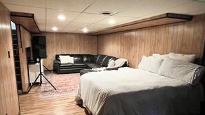 A bedroom with a large bed, a black leather sofa, and a wooden floor. - Cozy home in a peaceful country setting with stocked pond. Relax and unwind. (Bridgeport)