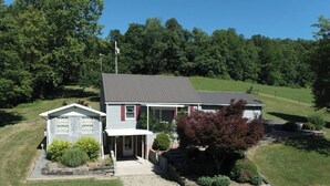 A two-story house with a front porch, a small attached garage, and a well-maintained lawn. - Cozy home in a peaceful country setting with stocked pond. Relax and unwind. (Bridgeport)