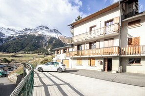 A two-story building with a balcony, a car parked in front, and a mountain in the background. - Chalet Faviere - VAL Cenis (VAL CENIS)