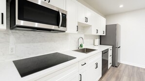 Una cocina moderna con armarios blancos, un microondas de acero inoxidable, un lavamanos y un refrigerador.