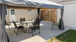 Un patio al aire libre con mesa y sillas, una parrilla y un área cubierta con cortinas.