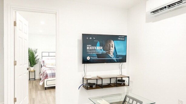 Una sala de estar moderna con un televisor de pantalla plana montado en la pared, una mesa de centro de vidrio y un sofá gris.