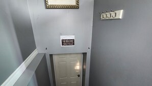 Un escalier avec une porte en bas, une pancarte de bienvenue et un porte-manteau fixé au mur.