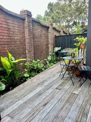Relax on the deck surrounded by lush greenery and a brick wall.