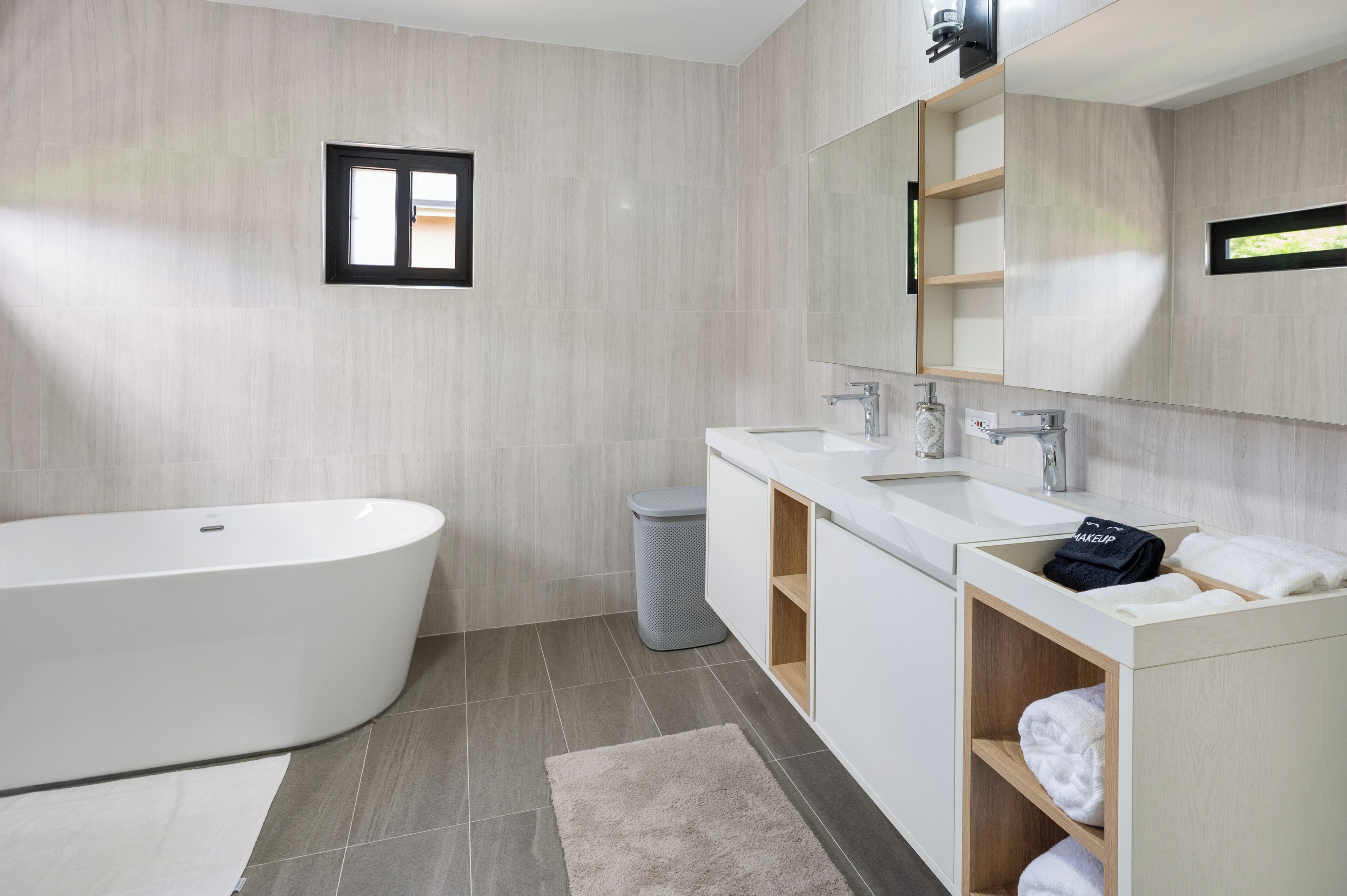 A modern bathroom with a freestanding bathtub, two sinks, and a large mirror.