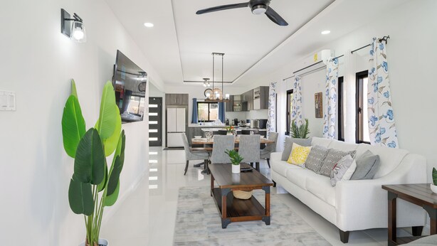 A modern living room with a white sofa, a dining table, and a large potted plant. - Beautiful Modern Vacation Home (Ocho Rios)