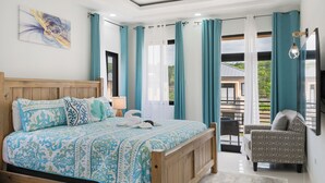 A bedroom with a wooden bed, teal curtains, and a view of the outdoors. - Beautiful Modern Vacation Home (Ocho Rios)
