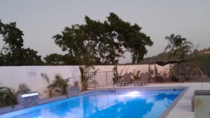 A swimming pool with a tiled deck, surrounded by palm trees and a covered seating area. - Beautiful Modern Vacation Home (Ocho Rios)