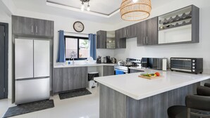 A modern kitchen with grey cabinetry, a large island, a microwave, a toaster, and a clock on the wall. - Beautiful Modern Vacation Home (Ocho Rios)