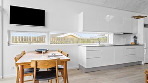 Une cuisine moderne avec des meubles blancs, un four encastré et une fenêtre donnant sur une clôture en bois.