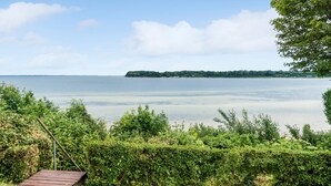 Une terrasse en bois surplombant un lac paisible, avec une île lointaine et une végétation luxuriante.