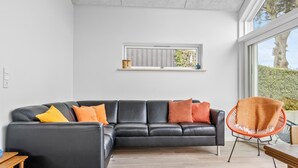 Un salon moderne avec un canapé en cuir noir, des coussins orange, une table basse en bois et un fauteuil en osier.