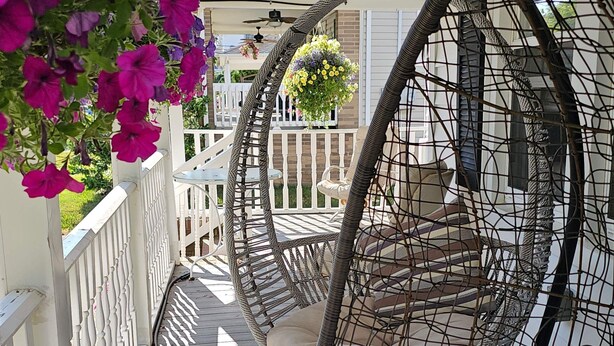 A porch with a hanging chair, a white fence, and a hanging flower basket.