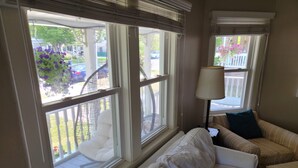 A room with a white sofa, a striped armchair, and a lamp. There are large windows with a view of a balcony and outdoor furniture.