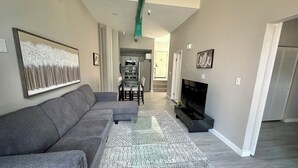 A modern living room with a grey sectional sofa, a glass coffee table, and a flat-screen TV. - NEW Cozy Apt Bright + Modern W/D (Albany)