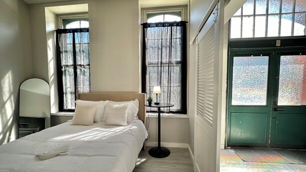 A bedroom with a bed, a bedside table, a lamp, and a window with curtains. - NEW Cozy Apt Bright + Modern W/D (Albany)
