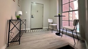 A room with a large window, a door, a small table with a plant, a chair, and a floor lamp. - NEW Cozy Apt Bright + Modern W/D (Albany)