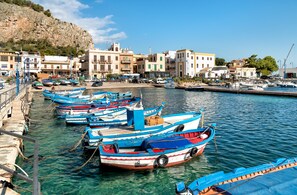 A marina with several small boats docked along the waterfront, surrounded by buildings and a rocky hillside.