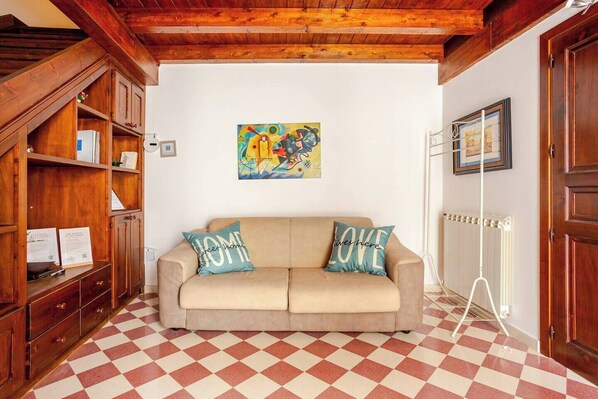 A cozy room with a checkered floor, a beige sofa with two pillows, wooden cabinets, and a radiator.