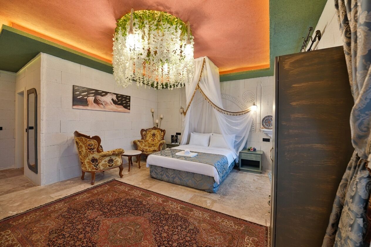 A bedroom with a bed, a chair, a table, a hanging floral chandelier, and a painting on the wall.
