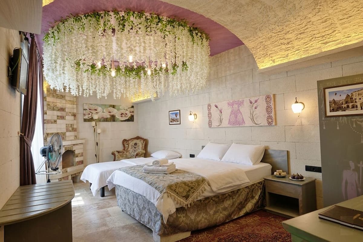 Ein Schlafzimmer mit zwei Betten, einem Kamin, einer blumigen Pendelleuchte und Wandleuchten.